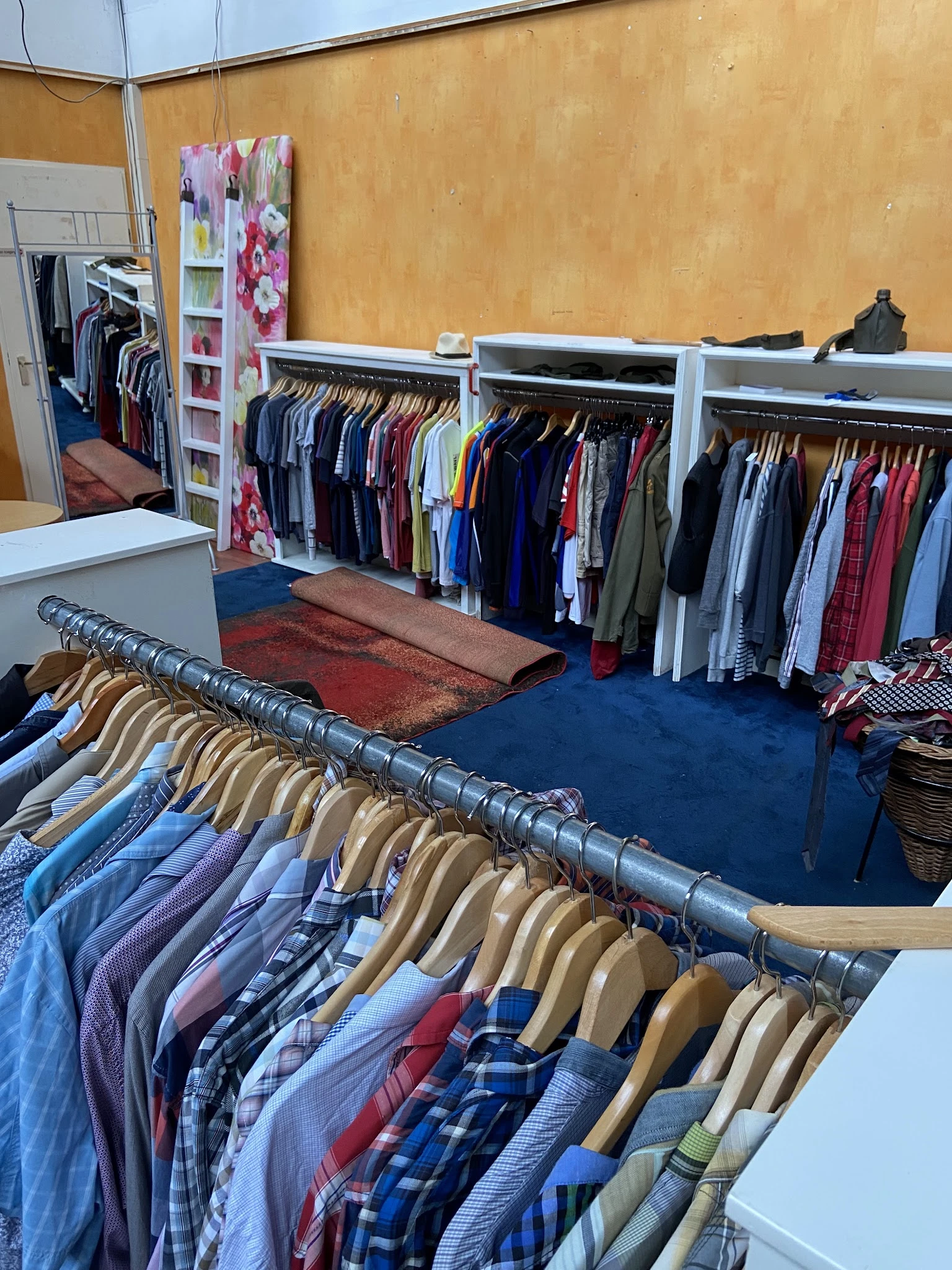 Rekken met tweedehands kleding, waaronder broeken en jasjes op hangers in een kringloopwinkel