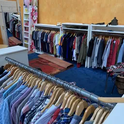 Rekken met tweedehands kleding, waaronder broeken en jasjes op hangers in een kringloopwinkel