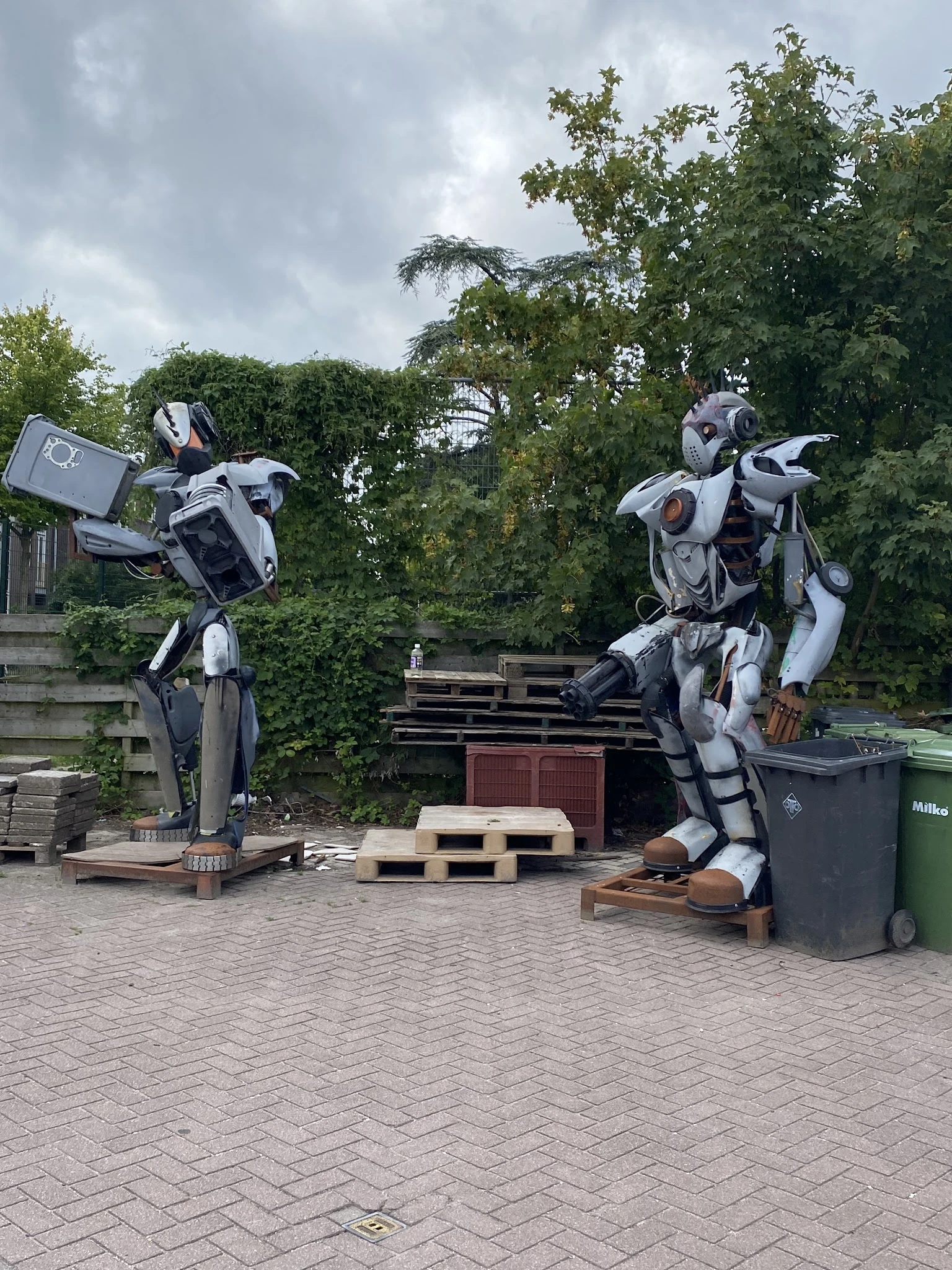 Twee grote witte en zwarte robotfiguren in een parkeerterrein met bomen op de achtergrond