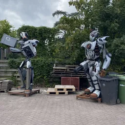 Twee grote witte en zwarte robotfiguren in een parkeerterrein met bomen op de achtergrond