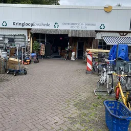 Voorgevel van kringloopwinkel met ingang, houten luifel en fietsen ernaast