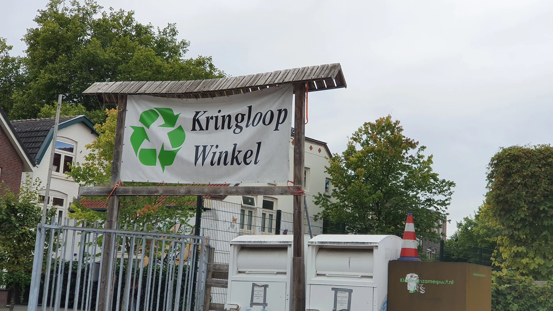 Uithangbord met groen recyclesymbool en winkelnaam, stellages met afvalbakken ervoor