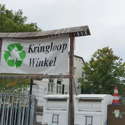 Uithangbord met groen recyclesymbool en winkelnaam, stellages met afvalbakken ervoor