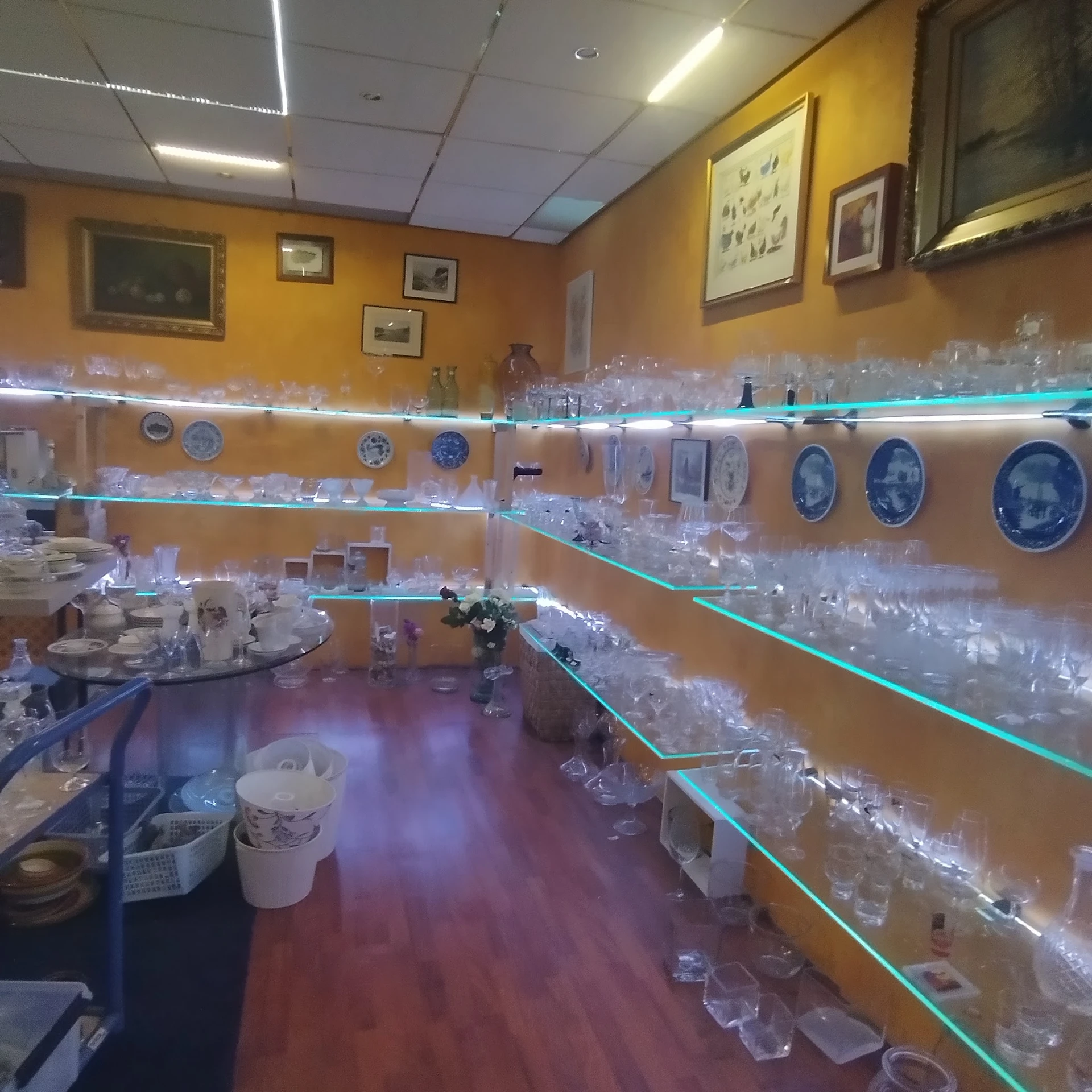 Glazen vitrinekasten met serviesgoed, porseleinen bordjes en glazen tegen gele muur