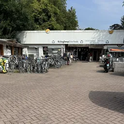 Voorgevel van kringloopwinkel met winkelnaam op luifel, fietsenrek en ingang zichtbaar