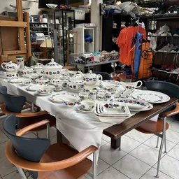 Tafelscène met serviesgoed: borden, kopjes en schalen met bloemendessin uitgestald op tafels met witte tafelkleden.