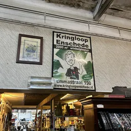Winkelinterieur met aan muur bevestigd reclamebord van Kringloop Enschede en enkele wanddecoraties
