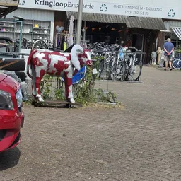 Voorkant van kringloopwinkel met fietsenrek en kunstobject op straat