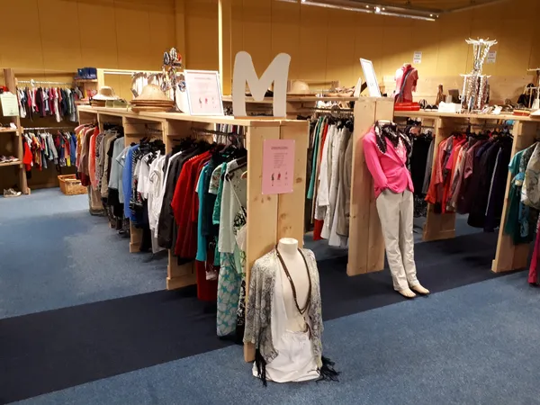 Winkelvloer met houten stellingen vol tweedehands kleding, mannequins en displaypoppen met opgehangen kledingstukken