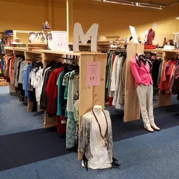 Winkelvloer met houten stellingen vol tweedehands kleding, mannequins en displaypoppen met opgehangen kledingstukken
