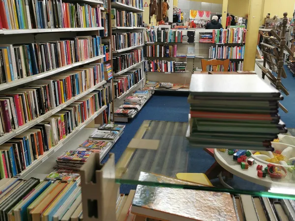 Binnenaanzicht van kringloopwinkel met boekenrekken, media-afdeling en uitgestalde spullen op de vloer
