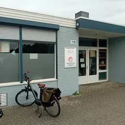 Gevel van kringloopwinkel met blauwe gevelsteen, glazen deuren en ramen, huisnummer 118, met fiets vooraan geparkeerd