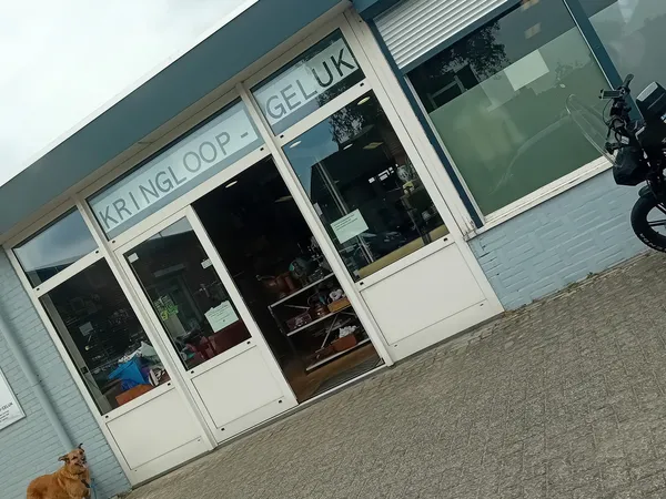 Witte gevel van kringloopwinkel met grote ramen en deuren, winkelnaam zichtbaar