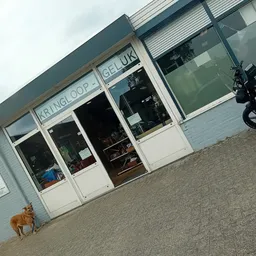 Witte gevel van kringloopwinkel met grote ramen en deuren, winkelnaam zichtbaar