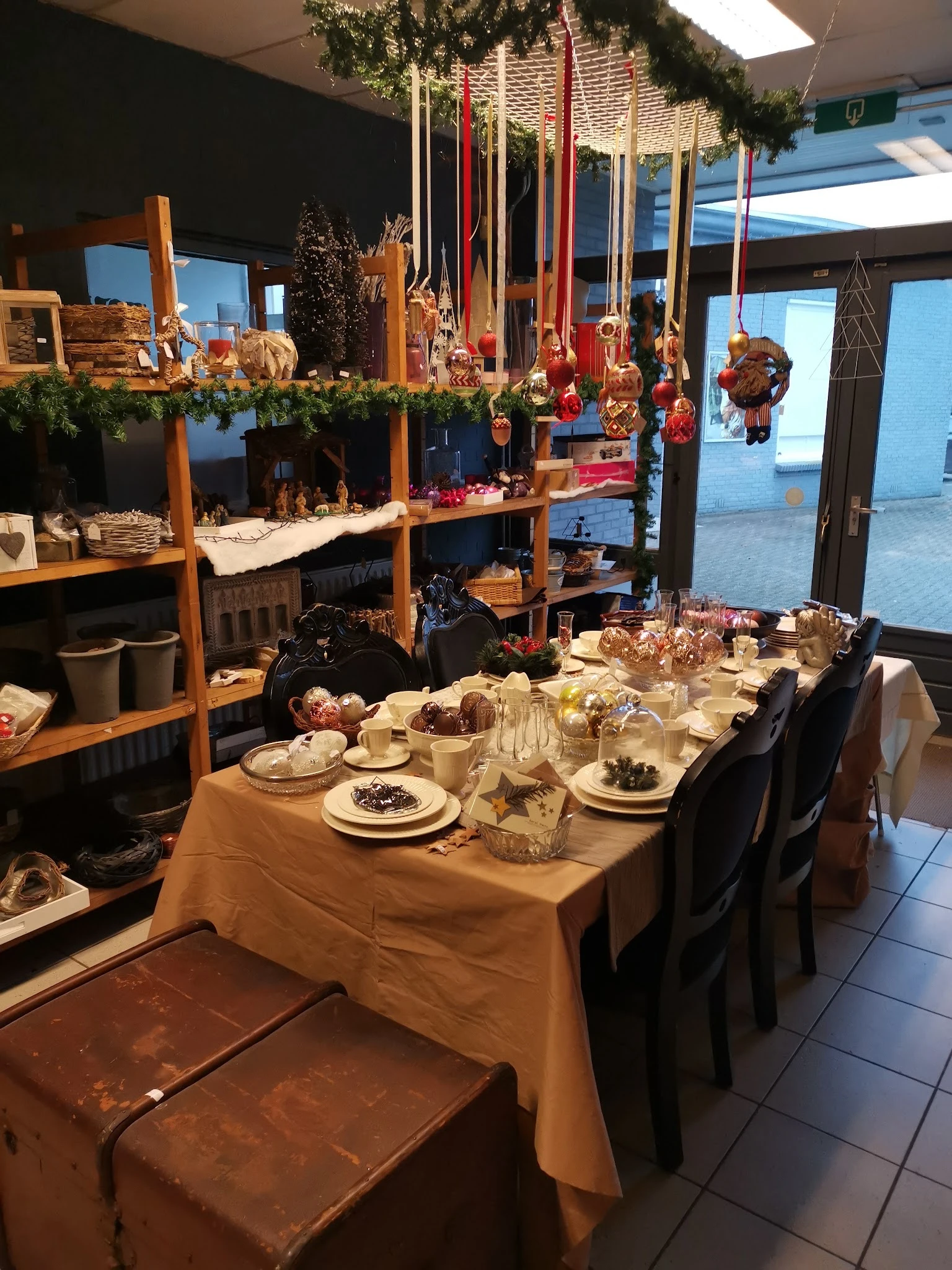 Gedekte tafel met borden, glazen en eten in een ruimte met grote ramen en kerstversiering