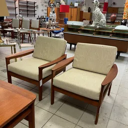 Twee vintage fauteuils met houten frame en beige stoffen bekleding naast elkaar in de winkel