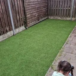 Achtertuin met kunstgras, houten schuttingen en plaveisel