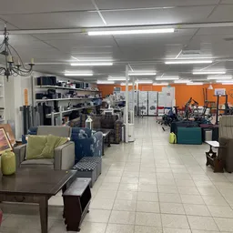 Ruime kringloopwinkel met meubels, huishoudspullen en decoratie uitgestald, oranje muren en fluorescente verlichting