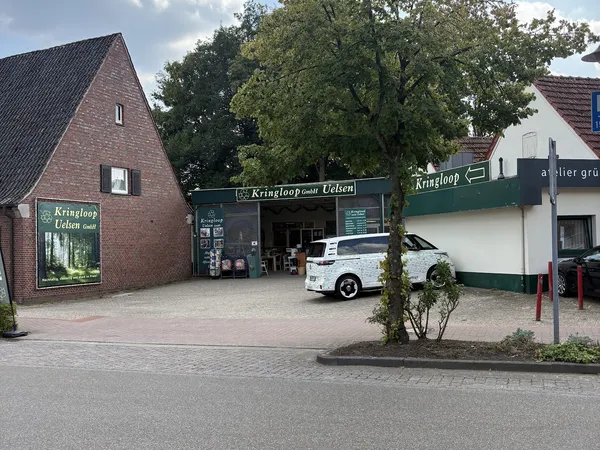 Voorgevel van kringloopwinkel Kringloop Uelsen met bakstenen pand, groene luifel en witte auto op parkeerplaats