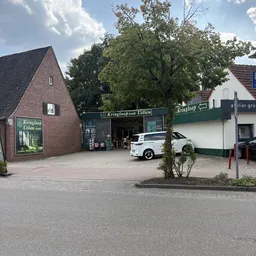 Voorgevel van kringloopwinkel Kringloop Uelsen met bakstenen pand, groene luifel en witte auto op parkeerplaats