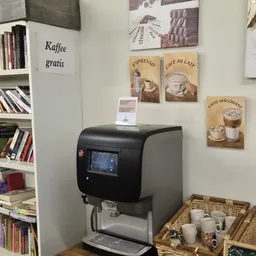 Automatische koffiemachine in een hoek met koffieposter's aan de muur en kopjes in een mand