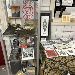 Vitrinekast en tafel met tweedehands boeken, vinyl, kunstprints en diverse items uitgestald