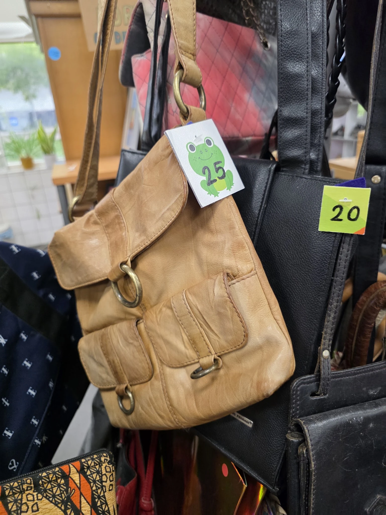 Beige leren schoudertas met prijskaartjes aan hangers in de winkel