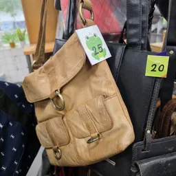 Beige leren schoudertas met prijskaartjes aan hangers in de winkel