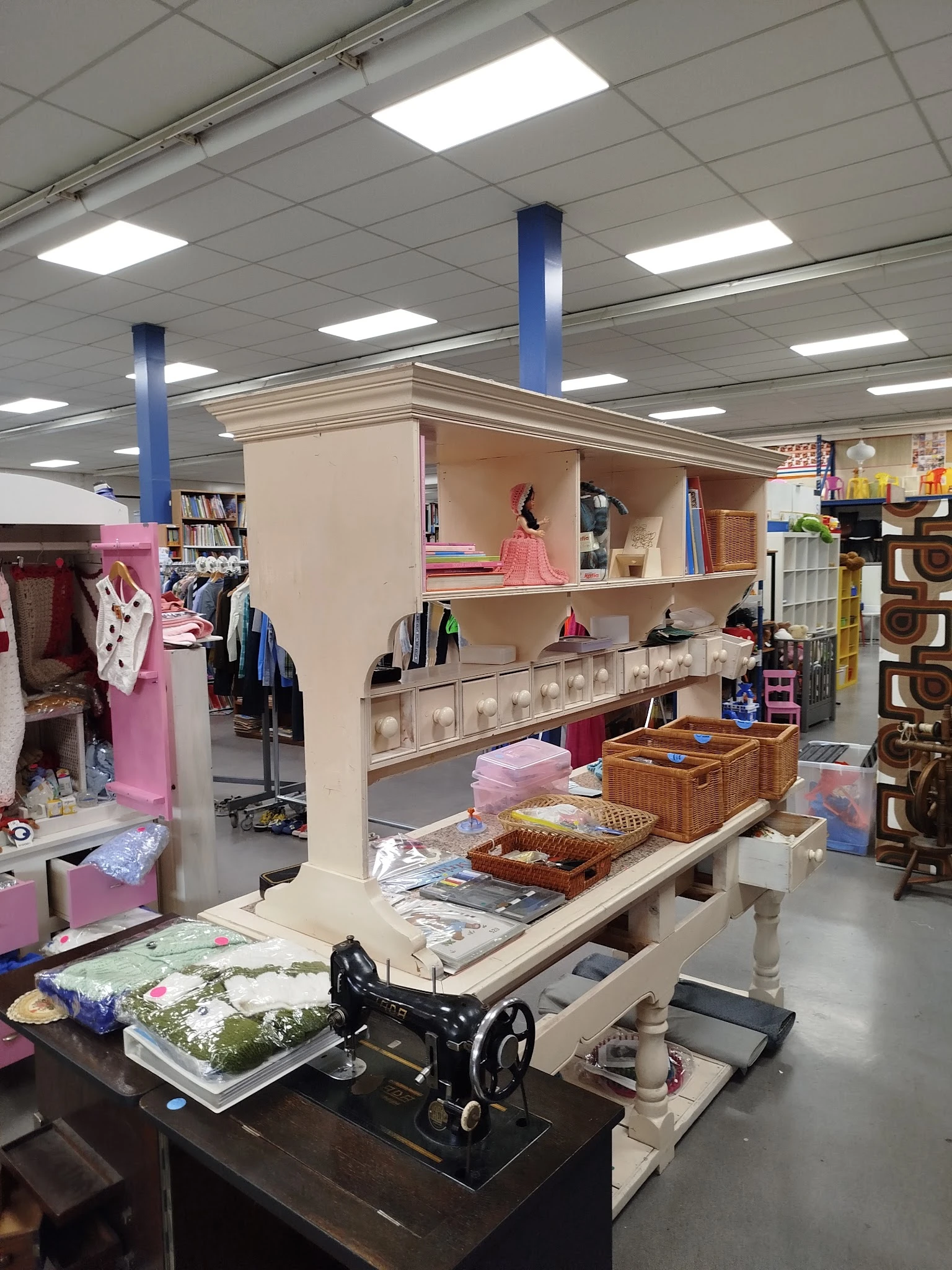 Winkelvloer met stellingen, kleding aan rekken, opbergkuipen en decoratieve items in een kringloopwinkel