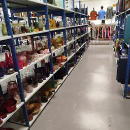 Gangpad tussen blauwe stellingen met huishoudelijke spullen en kleding in kringloopwinkel