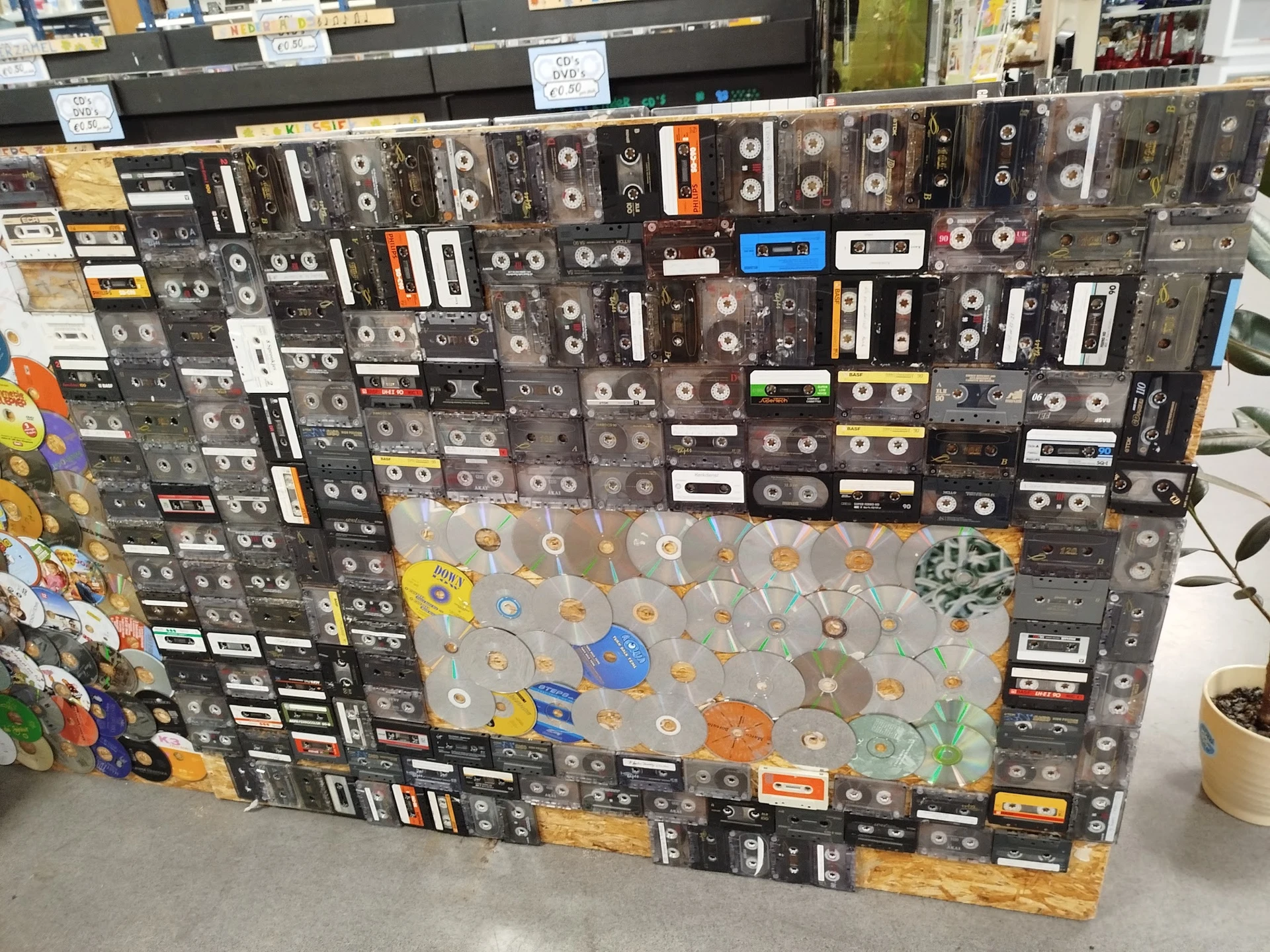 Grote collectie cassettebandjes en cd's uitgestald op een zwart panneel in de winkel