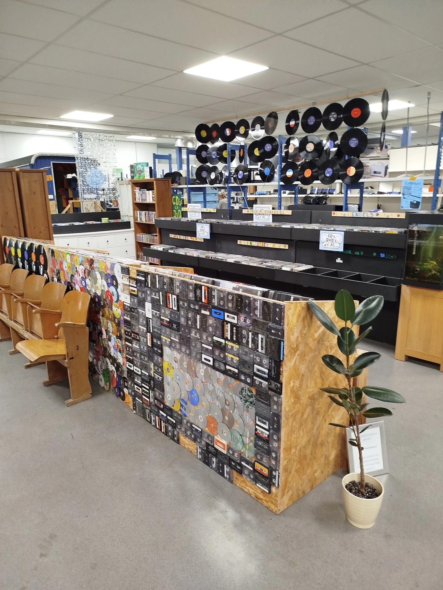 Winkelvloer met diverse spullen, waaronder vinyl records aan het plafond, een zwart bureau/werkplek, houten meubels en een de
