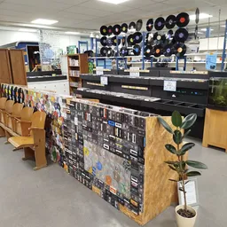 Winkelvloer met diverse spullen, waaronder vinyl records aan het plafond, een zwart bureau/werkplek, houten meubels en een de