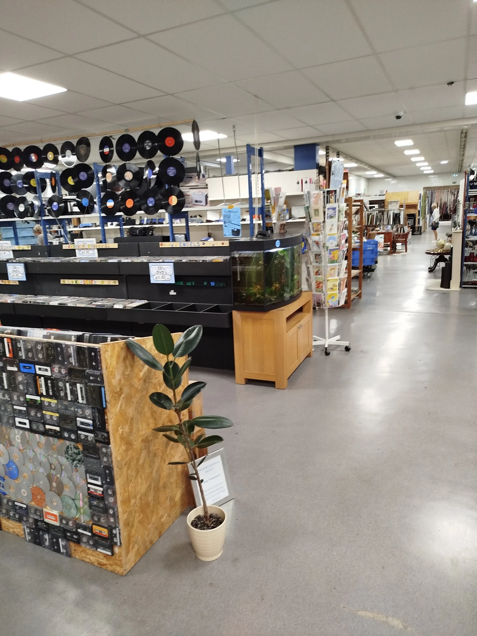 Winkelvloer van kringloopcentrum met piano, aquarium, vinyl records, plantenstandaard en diverse kringloopwaar