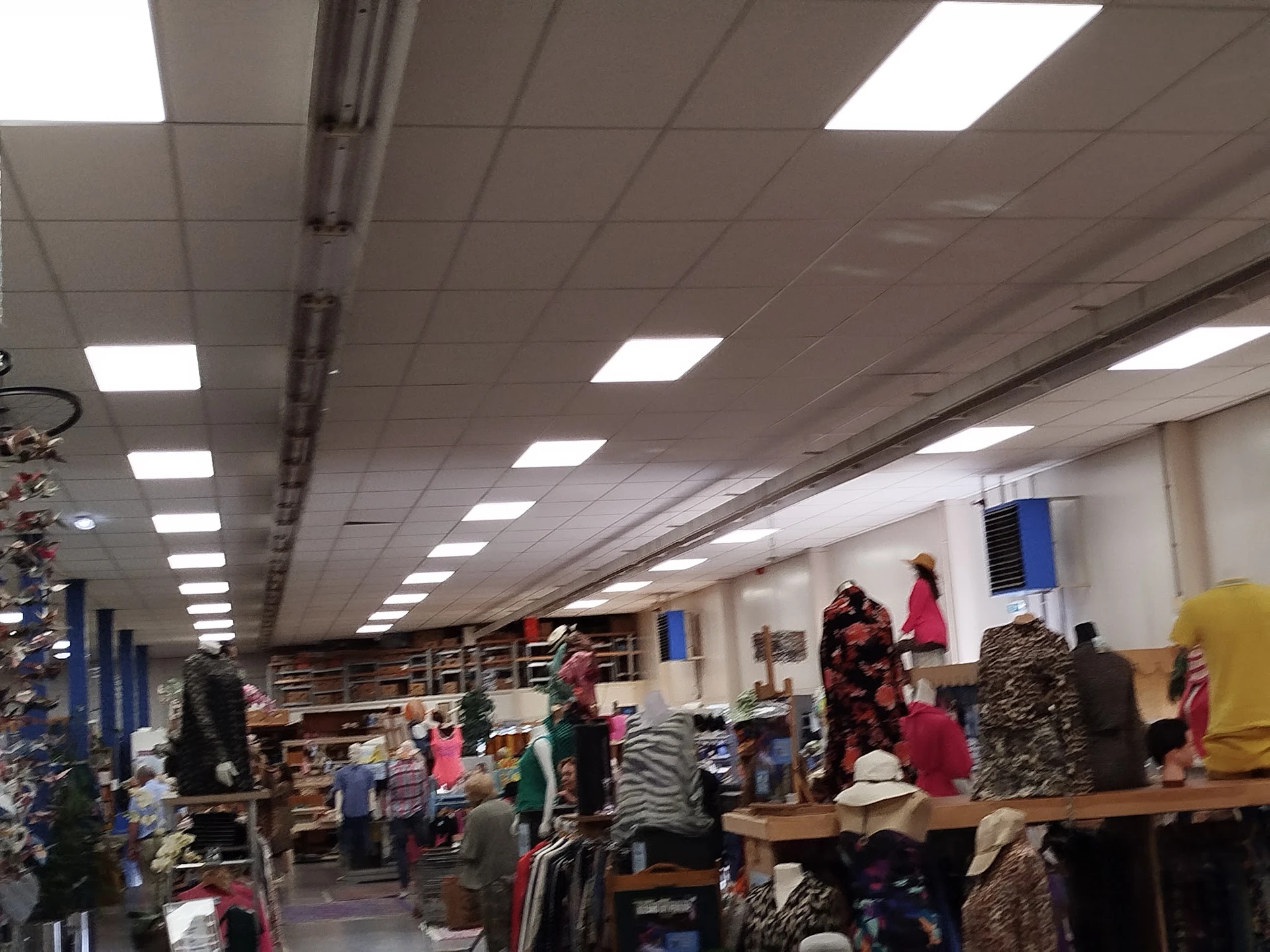 Winkelvloer van kringloopwinkel met kleding op tafels en rekken, bezoekers aan het winkelen