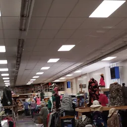 Winkelvloer van kringloopwinkel met kleding op tafels en rekken, bezoekers aan het winkelen