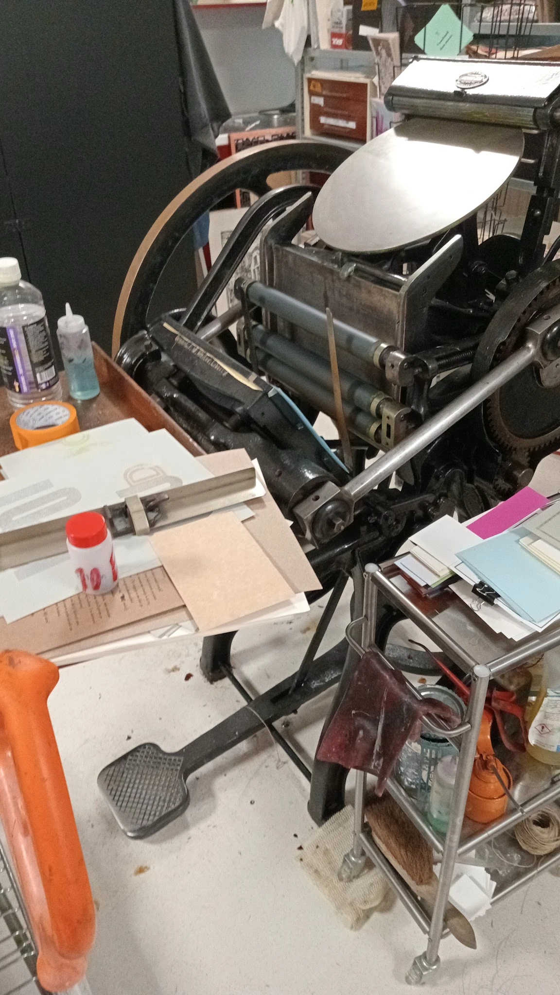 Verzameling tweedehands artikelen op tafel: printermachine, papier, flessen en diverse kantoorspullen
