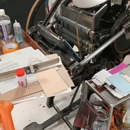 Verzameling tweedehands artikelen op tafel: printermachine, papier, flessen en diverse kantoorspullen
