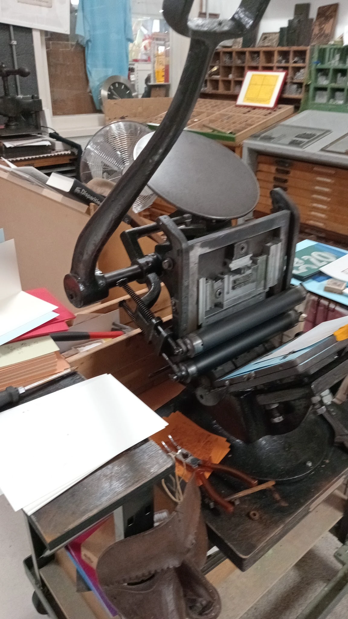 Close-up van een zwarte papiersnijmachine op een houten werkblad met papier en andere spullen eromheen