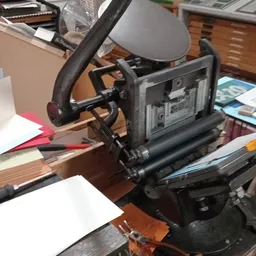 Close-up van een zwarte papiersnijmachine op een houten werkblad met papier en andere spullen eromheen