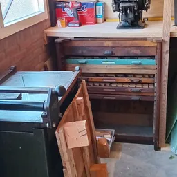 Houten meubel met uitschuifbare laden in verschillende kleuren, gedeeltelijk geopend in een kringloopwinkel