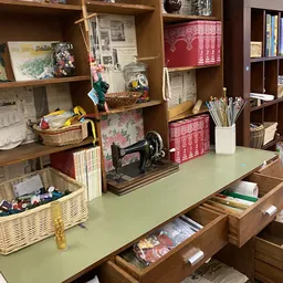 Winkelinterieur met houten stellingen vol spullen, bureauwerk en decoratie; op de tafel staat een oude naaimachine