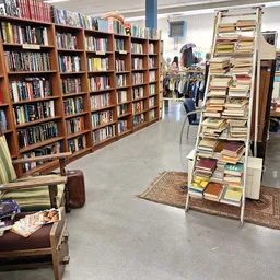Winkelvloer met houten boekenkasten vol boeken, een leeszetel, en een bewegwijzering naar het kledinggedeelte