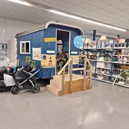 Winkelvloer met blauwe aanhangwagen, kinderwagen, houten speeltoestel en rekken met spullen