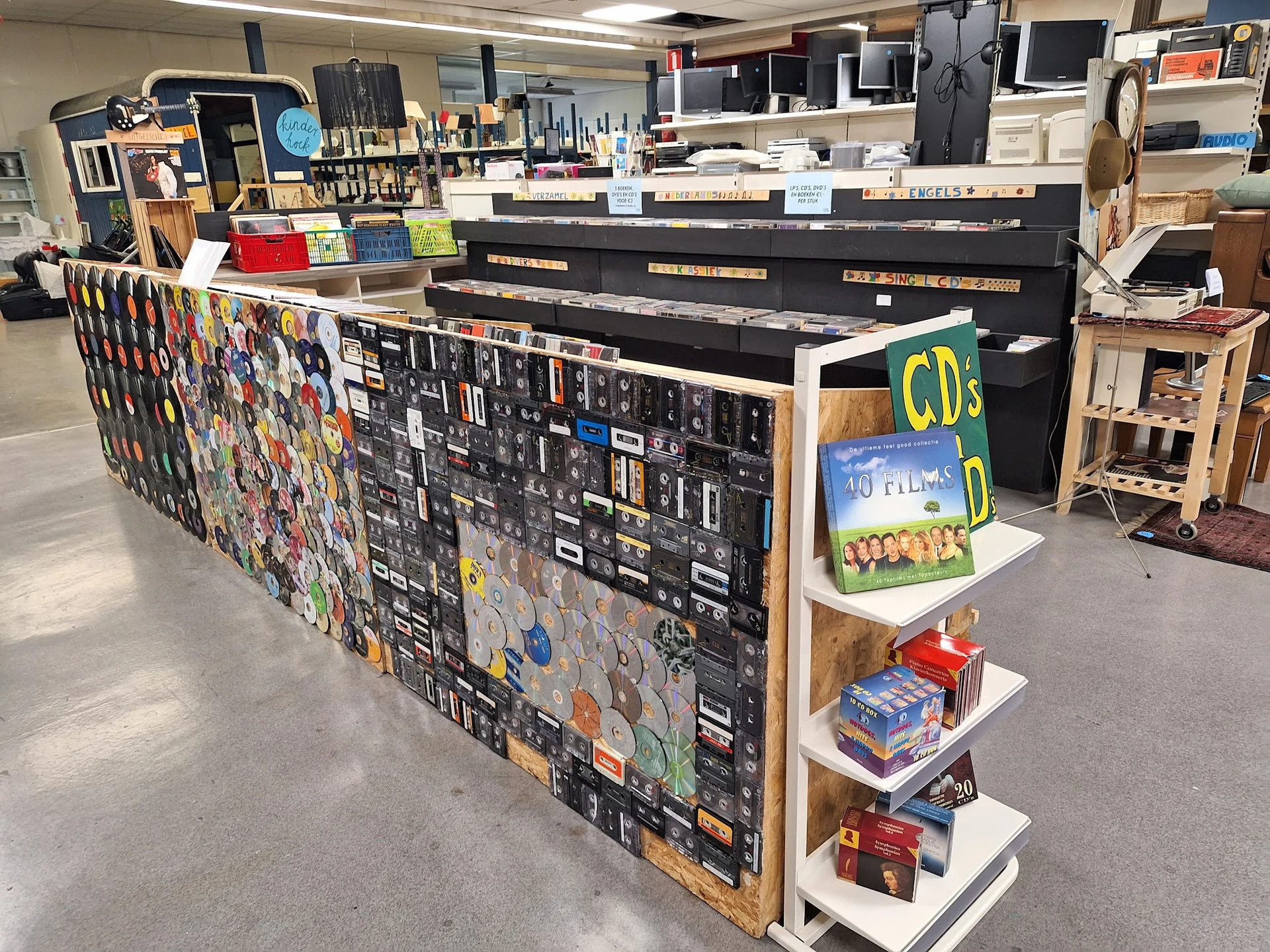 Winkelinterieur met een grote toonbank versierd met stickers, CDs en ander tweedehandsaanbod op planken