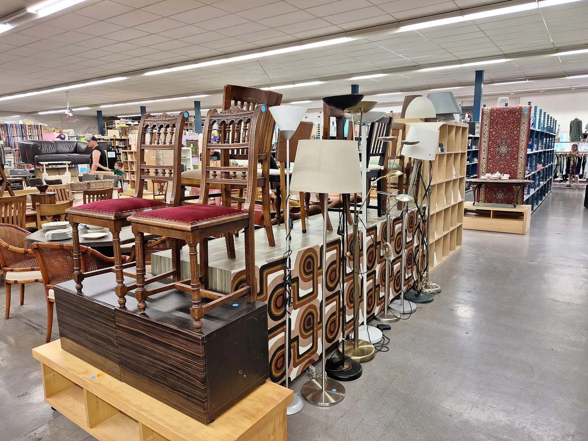 Uitgestalde meubels in kringloopwinkel: houten tafels, stoelen, kasten en decoratieve artikelen op verschillende displays.