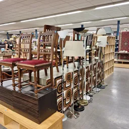 Uitgestalde meubels in kringloopwinkel: houten tafels, stoelen, kasten en decoratieve artikelen op verschillende displays.