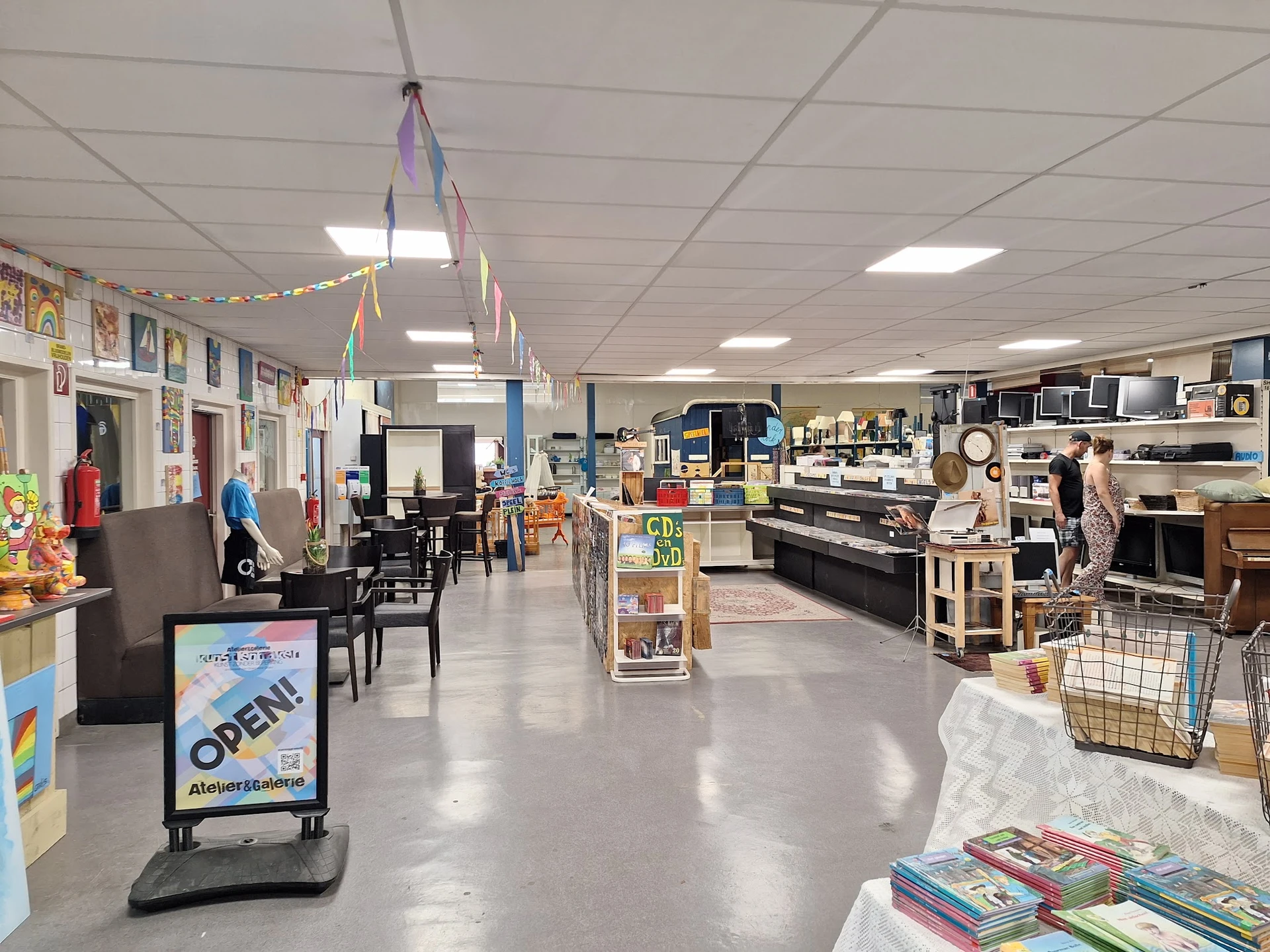 Ruim winkelinterieur met diverse afdelingen: meubilair, boeken, huishoudartikelen en decoraties verspreid over de vloer