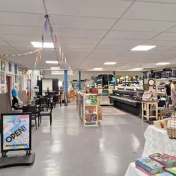 Ruim winkelinterieur met diverse afdelingen: meubilair, boeken, huishoudartikelen en decoraties verspreid over de vloer
