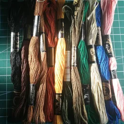 Uitgestalde borduurgarens in verschillende kleuren op een groene snijmat